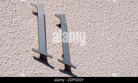 Eine weiße Mauer und Hausnummer 11 und der Schatten dieser Zahl an der Wand Stockfoto