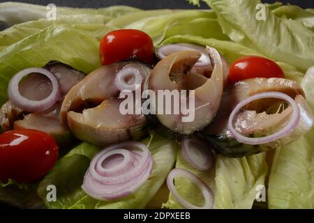 Scheiben von kalt geräuchertem Makrelenfisch, mit Kirschtomaten und roten Zwiebeln auf Salatblättern. Stockfoto