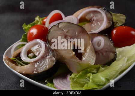 Scheiben von kalt geräuchertem Makrelenfisch, mit Kirschtomaten und roten Zwiebeln auf Salatblättern. Stockfoto