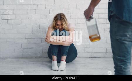 Alkoholismus und häusliche Gewalt. Aggressiver Mann mit Flasche bedroht verängstigte Frau Stockfoto