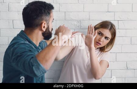 Ehemann schlägt seine Frau zu Hause. Wütender Mann hebt seine Faust auf verängstigte Frau Stockfoto