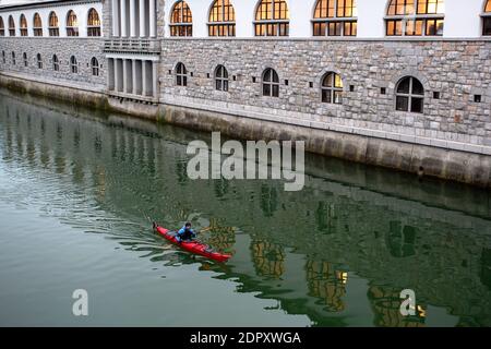 Kayaker in se Kajak Kajakfahren auf Ljubljanica Fluss mit Plecnik Central Market im Hintergrund im Winter, Ljubljana, Slowenien Stockfoto