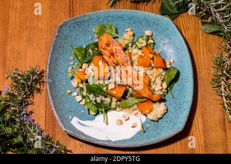 Typischer Fisch frischer Teller, leckerer gegrillter Lachs mit gegrillten Kürbissen und Joghurtsauce auf einem schicken Holztisch. Mediterrane Gerichte mit einem Stockfoto