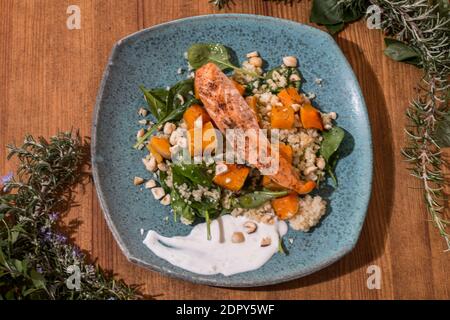 Typischer Fisch frischer Teller, leckerer gegrillter Lachs mit gegrillten Kürbissen und Joghurtsauce auf einem schicken Holztisch. Mediterrane Gerichte mit einem Stockfoto