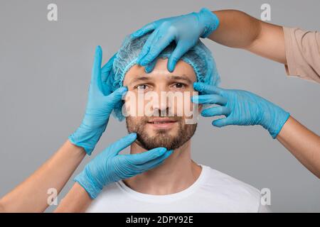Ärzte Hände in Schutzhandschuhen berühren Mann Gesicht vor der Operation Stockfoto