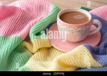 Gestrickte Tasse Kaffee oder Cappuccino auf bunt gestricktem Karo. Good Morning Konzept. Stockfoto