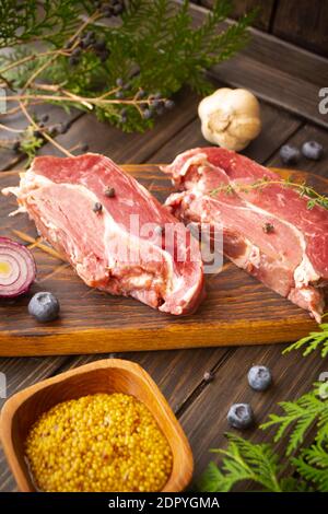 Frisches Fleisch von Wildschweinen auf dem Brett zum Schneiden mit Heidelbeeren und einer Knoblauchzwiebel, vertikales Bild Stockfoto