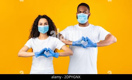 Paar Gestikulierenden Herzform Tragen Masken Und Handschuhe, Gelber Hintergrund Stockfoto