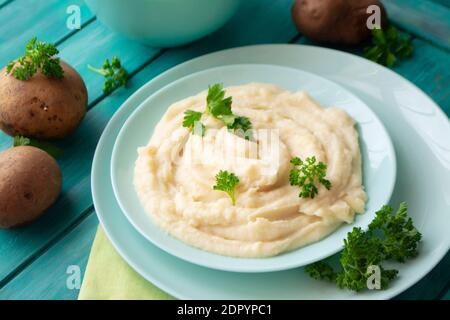 Leckere Kartoffelpüree mit grüner Petersilie in einer türkisfarbenen Schüssel mit Gemüse. Stockfoto