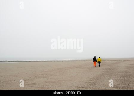 Zwei Menschen gehen an einem Sandstrand im Nebel, Nordsee, Norderney, Niedersachsen, Deutschland Stockfoto