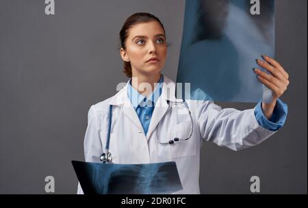 Eine Frau in einem medizinischen Kleid untersucht Röntgenstrahlen auf einem Grauer Hintergrund Stockfoto