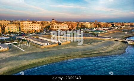 Sonnenuntergang Rom Luftaufnahme in Ostia Lido Strand über blau Meer mit Skyline der Stadt und Blick auf den Ravennati Platz und Fußgängerpier ein Wahrzeichen der Touristen und Stockfoto