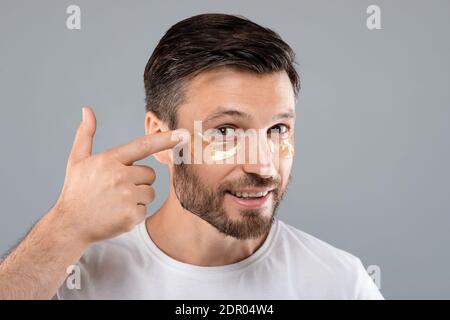 Hübscher Mann, der Augenflecken auf sein Gesicht anwendet Stockfoto