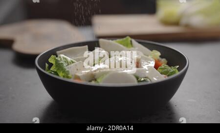 Würzsalat mit Rosensalat, Tomaten und Mozzarella in schwarzer Schüssel auf Betonplatte, breites Foto Stockfoto