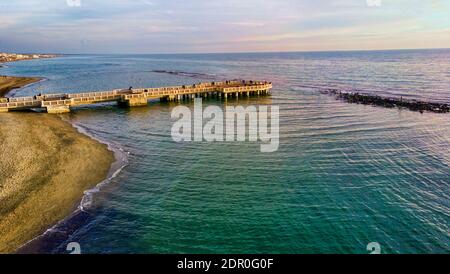 Sonnenuntergang Rom Luftbild in Ostia Lido Strand über blauem Meer und braunem Sand, schöne Küste mit Blick auf Fußgängerpier ein Wahrzeichen der Touristen ein Stockfoto