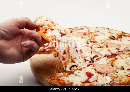 Die Hand des Mannes nimmt ein köstliches Stück Pizza mit Margarita oder Margarita mit Mozzarella, EIN Mann nimmt ein Stück italienische Pizza und zieht einen appetitlich geschmolzenen Käse. Stockfoto