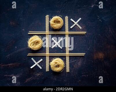 Verschiedene Arten von getrockneten Pasta in tic tac Toe Spiel auf dunklen vintage Hintergrund. Overhead-Aufnahme mit Kopierplatz. Knolling-Konzept. Stockfoto