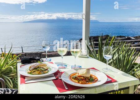 Teller mit Fisch, Seebarsch und Seehecht mit Gläsern Weißwein auf einem Tisch im Restaurant Pergola am Meer in Puerto Santiago, Teneriffa, Kanarische Stockfoto