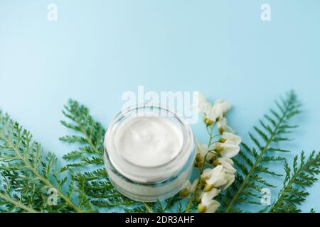 Gesichtscreme und schöne weiße Blumen auf blauem Hintergrund mit Grün mit einem Kopierraum. Stockfoto