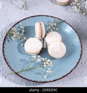 Vanillemakronen auf einem blauen Teller, Blumen im Hintergrund Stockfoto