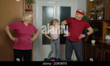 Enkelin und ältere Großeltern in Sportbekleidung machen Sport-Training zu Hause. Aktive kaukasischen Senior paar Großmutter Großvater mit Kind Kind Mädchen tun Fitness-Übungen während Coronavirus Stockfoto