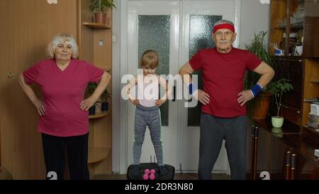 Aktive kaukasischen Senior paar Großmutter Großvater mit Kind Kind Mädchen tun Stretching-Übungen. Enkelin und ältere Großeltern in Sportbekleidung machen Sport-Training zu Hause in Quarantäne Stockfoto