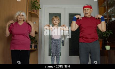 Aktive kaukasischen Senior paar Großmutter Großvater mit Kind Kind Mädchen tun Stretching-Übungen. Enkelin und ältere Großeltern in Sportbekleidung machen Sport-Training zu Hause in Quarantäne Stockfoto