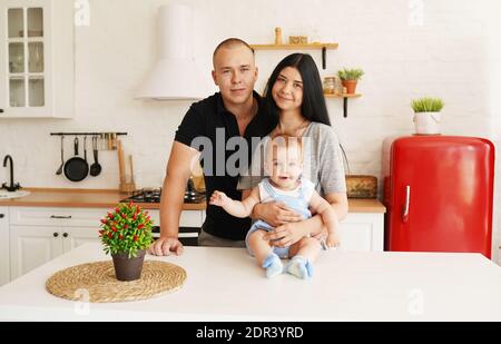 Familienportrait in der Küche: Mutter, Vater und netter kleiner Junge, der Kamera anschaut und lächelt Stockfoto