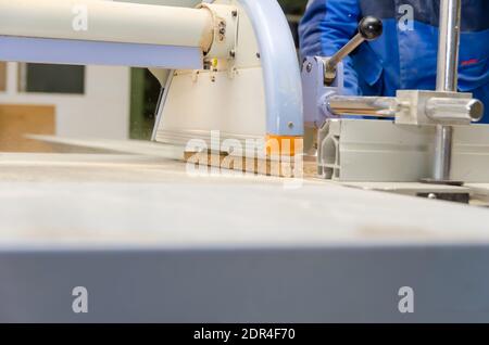 Männlicher Mitarbeiter steht hinter einer Formatschneidemaschine für die Holzbearbeitung. Holzbearbeitungsmaschine in einer Schreinerei Stockfoto