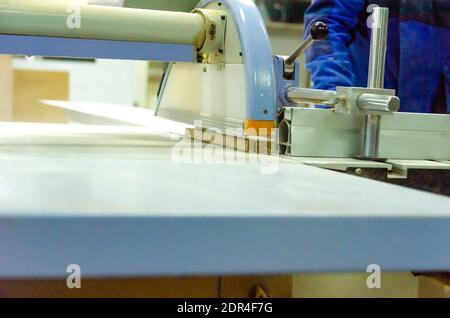 Männlicher Mitarbeiter steht hinter einer Formatschneidemaschine für die Holzbearbeitung. Holzbearbeitungsmaschine in einer Schreinerei Stockfoto