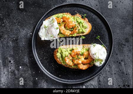 Toast mit Garnelen, Garnelen, Avocado und pochiertem Ei. Schwarzer Hintergrund. Draufsicht. Stockfoto