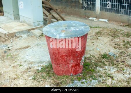 Zementeimer. Große Kapazität für Baustoffe. Roter Eimer mit Deckel. Verlassene Inventar auf der Straße. Ein Eimer Farbe. Stockfoto