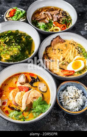 Verschiedene traditionelle asiatische Suppen. Miso, Ramen, Tom Yam, Pho Bo. Schwarzer Hintergrund. Draufsicht. Stockfoto