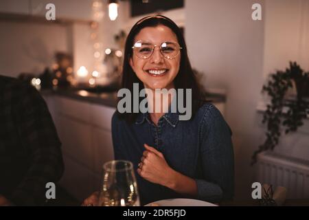 Junge Frau lächelt, während sie mit Freunden um ein Essen herum sitzt Tisch bei Kerzenschein Stockfoto