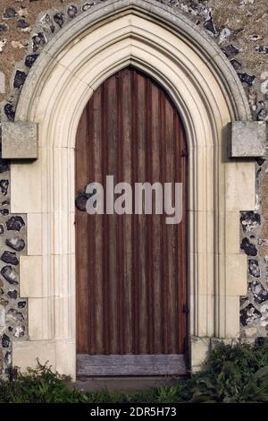 Vintage-Bogenholztür in einer Steinkirchenwand, St. Margaret's Church, Rottingdean, East Sussex, England, im vertikalen Format Stockfoto