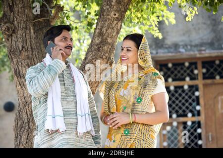 Ländliche indische Frau, die den Mann beim Telefonieren ansieht Stockfoto