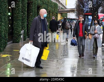 Ein Mann mit Gesichtsmask trägt Einkaufstaschen, als er das Kaufhaus Selfridges in der Oxford Street verlässt.Last-Minute-Weihnachtseinkäufe in Londons Oxford Street und Regent Street am Vorabend, in die Stufe 4-Sperre gestürzt zu werden, mit allen nicht notwendigen Einzelhandelsgeschäften, die geschlossen werden sollen. Stockfoto