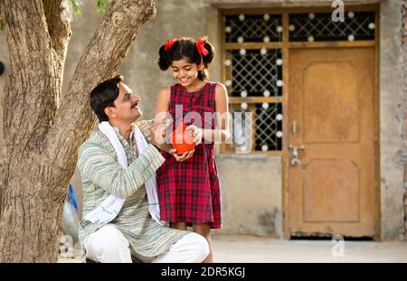 Ländlicher indischer Vater mit Tochter, die Sparschwein hält Stockfoto