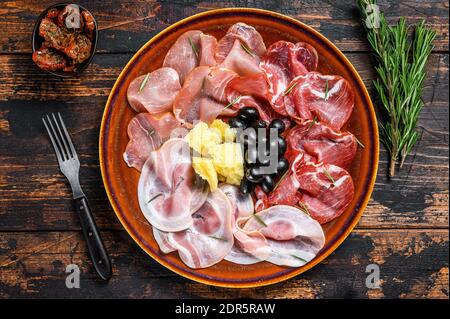 Italienische Fleischplatte mit Prosciutto-Schinken, bresaola, Pancetta, Salami und Parmesan. Dunkler Holzhintergrund. Draufsicht. Stockfoto