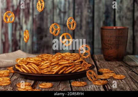 Levitation von Lebensmitteln. Kleine Plätzchen in Form von Brezeln, die in eine Tonschale fallen, Holzhintergrund. Stockfoto