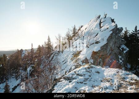 Riesiger Stein bedeckt mit Schnee auf dem felsigen Berg Umgeben von Bäumen Mischwald gegen blauen Himmel mit Sonnenschein am Wintertag Stockfoto