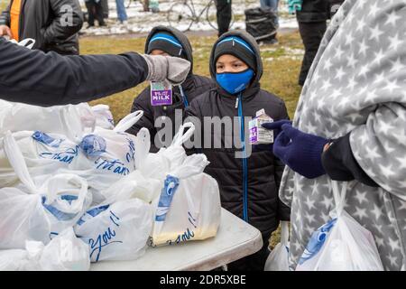 Detroit, Michigan, USA. Dezember 2020. In der Woche vor Weihnachten liefern Freiwillige im Roosevelt Park in Detroit Lebensmittel an bedürftige Menschen, die meisten von ihnen obdachlos. Kleine Jungen erhalten Milch als Teil ihrer Mahlzeit. Kredit: Jim West/Alamy Live Nachrichten Stockfoto