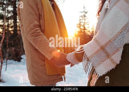 Seitenansicht von jungen liebevollen und lieblichen Datteln in Wintermode Stehen vor einander und halten an den Händen Im Wald am Winterwochenende Stockfoto