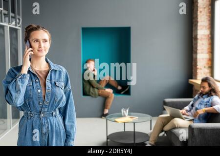 Junge beschäftigt weibliche Büroangestellte in Casualwear Beratung Client auf Mobiltelefon, während Sie mit Gadgets gegen zwei männliche Kollegen stehen Stockfoto