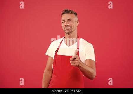 Glücklicher Unternehmer des Kaffeehaus. Der Barista ist männlich und trägt Uniform. Der unrasierte Mann arbeitet als Barista. Teilzeitjob. Selbstbewusster Barista Mann zeigt Finger. Reife erfahrene Barista tragen rote Schürze. Stockfoto