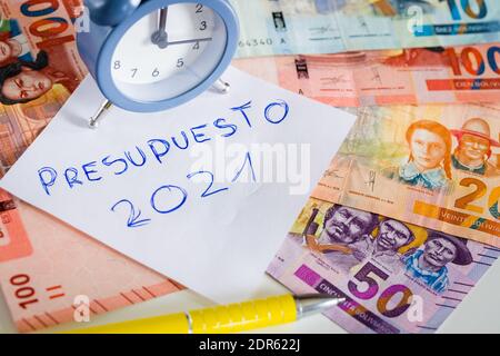 Stilvoller Wecker für fünf bis zwölf Personen. Im Hintergrund eine Brieftasche mit einem klebenden Stapel bolivianischen Geldes. Hundert Boliviano-Banknoten Stockfoto