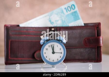 Stilvoller Wecker für fünf bis zwölf Personen. Im Hintergrund ragt eine Brieftasche mit einem Bündel brasilianischen Geldes hervor. Hundert Reais-Banknoten Stockfoto