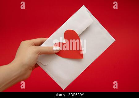 Frau Hand hält Umschlag mit Liebe in Form von roten valentine Herz auf rotem Hintergrund versiegelt. Valentinstag Stockfoto