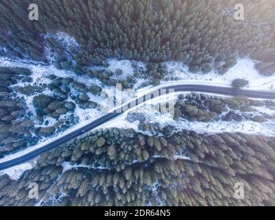 Schneebedeckte Tannebäume und Straße mit einem Fluss in den Bergen, Blick von oben. Winterwald und Straße von oben Stockfoto