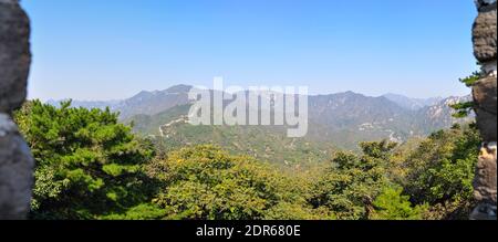 Panoramablick von der majestätischen Chinesischen Mauer auf die umliegende Landschaft und Wälder. Der Horizont ist im blauen Dunst. Bäume vor dem Hotel Stockfoto